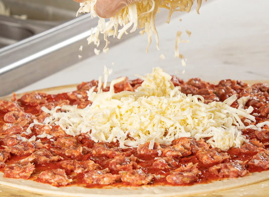 Pizza with cheese being sprinkled